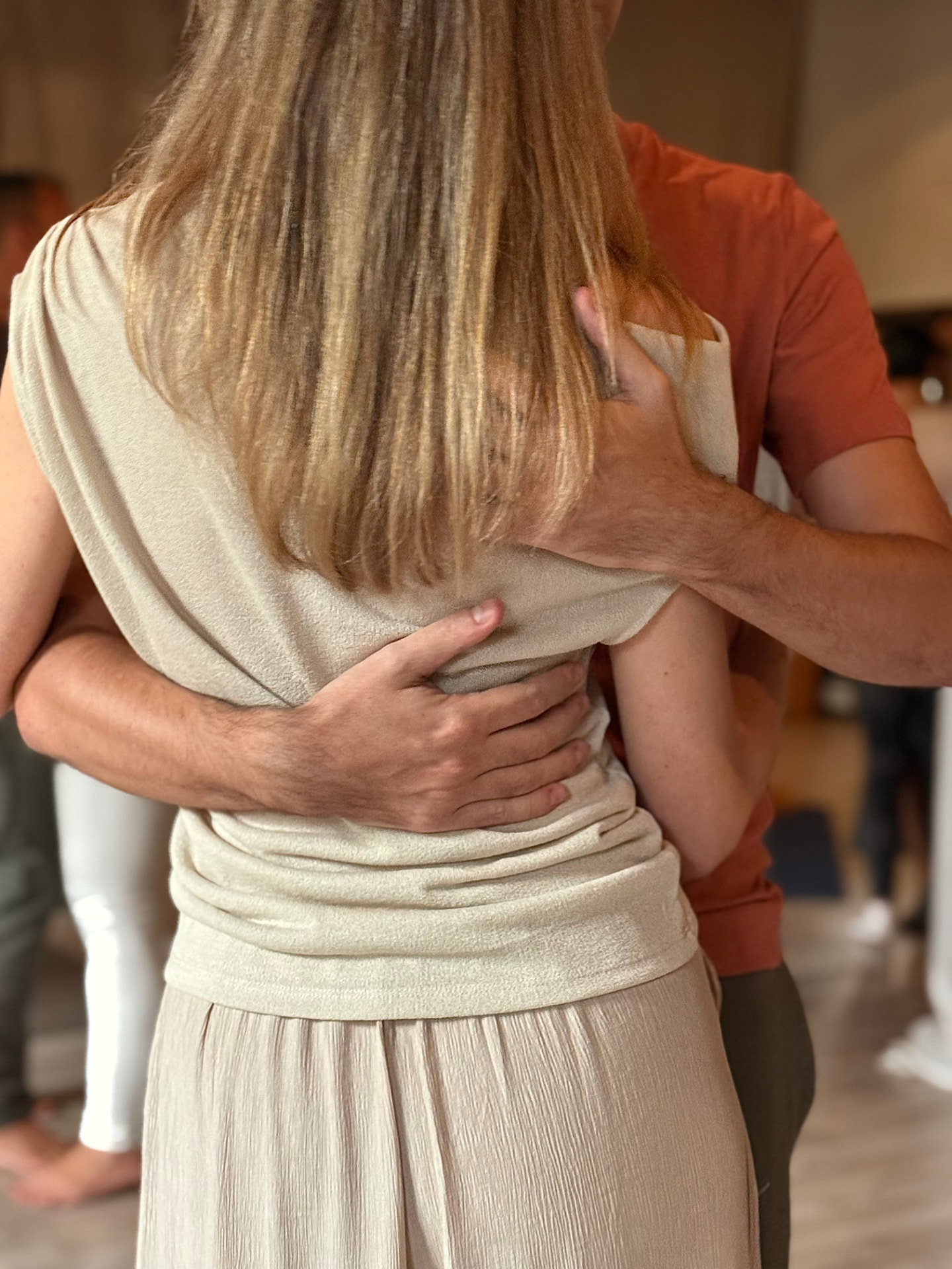 Two people embracing, hands resting on each other's shoulder blades